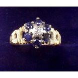 An 18 carat gold sapphire and diamond cluster ring on pierced textured shoulders, size M 1/2