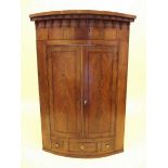 An early 19th century mahogany bow fronted corner cupboard with pendant frieze over two doors,