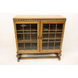 A Waring and Gillow oak glazed double door bookcase, with carved frieze, baluster supports on plinth