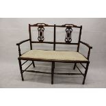 An Edwardian two seater settee, the pierced splats with stuffover seat on turned tapered supports,