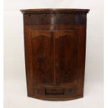 A Victorian mahogany barrel front hanging corner cabinet, having double doors over central drawer