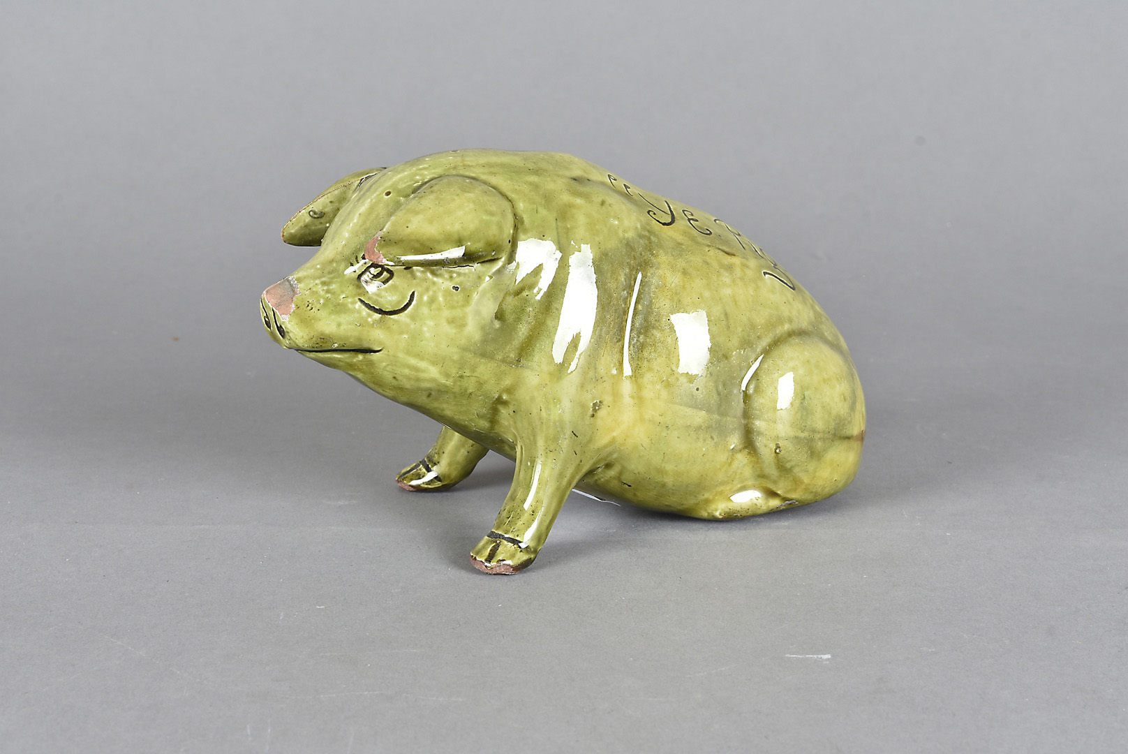A Ewenny pottery pig, seated, titled Ye Pig dated to base 1900 in green glaze, 17 cm long x 10 cm