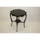 An Edwardian ebonised two tier occasional table, with shaped top, carved apron, cabriole scroll legs