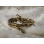 A 1980s 9ct gold serpent bracelet by C&F, the coiled snake having a pair of green stone eyes,