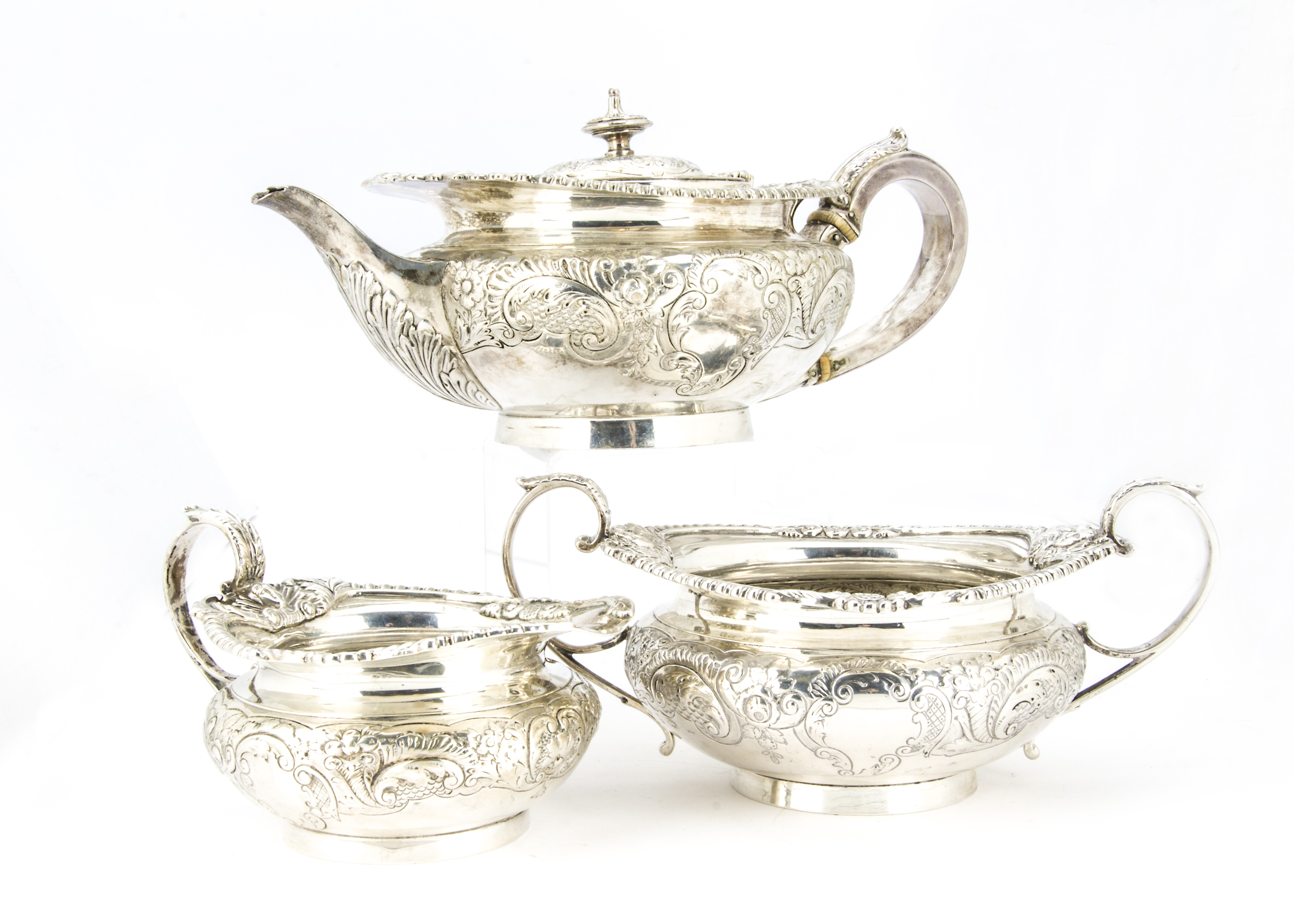 An Edwardian silver three piece tea set by Elkington & Co, squat form with ornate shell, mask and