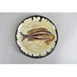 A early 20th Century stoneware iron and ash glazed studio plate, centred with fish design, having