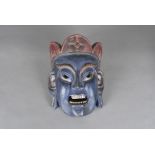 A carved Indian face mask, modelled as a blue faced god wearing red crown, with wax seal to verso,