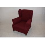 A 20th Century wing back armchair, upholstered in red pattern fabric, with turned front legs, on