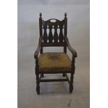 An Arts and Crafts oak elbow chair, with acorn finials, baluster-pattern back splat and patterned