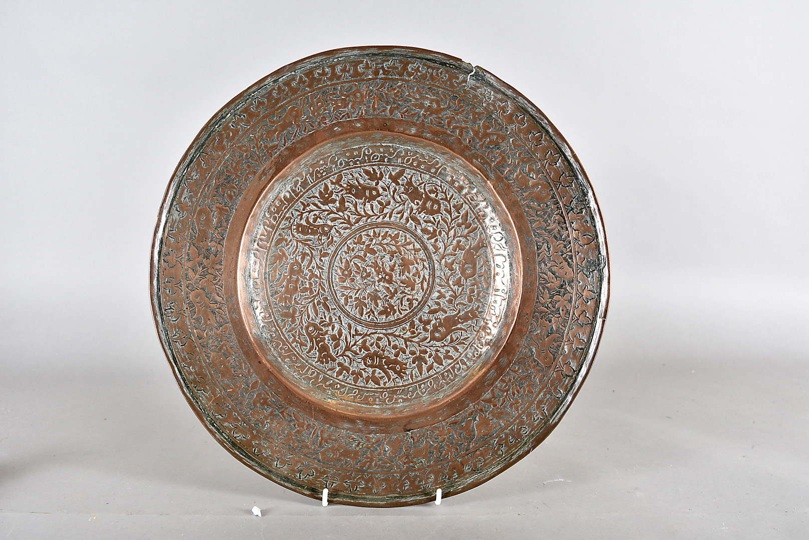 A middle eastern copper charger, decorated with stylised flowers and sunken centre, 39 cm diameter