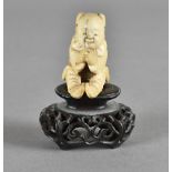 A Japanese Meiji period ivory carved netsuke, modelled as a seated boy inspecting his clasped hands,