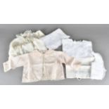 A collection of early 20th Century baby clothes and linen, including a Swiss made silk cardigan, a