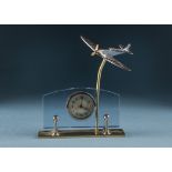 A 1950s Spitfire desk clock, the chromed Spitfire on brass support above glass and brass base with