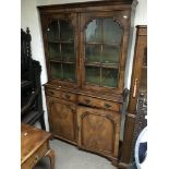 A two door walnut glazed display cabinet over two