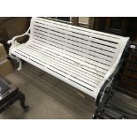 A white painted wrought iron garden bench with slatted wooden seat, the side pieces decorated with