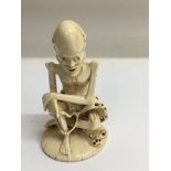 A carved ivory figure of a seated skeletal man holding a string of beads.Approx 15cm