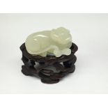 A further small light green carved jade model of a reclining dog, on carved wooden base. Approx 4cm