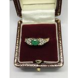 A gold ring set with a central emerald flanked by