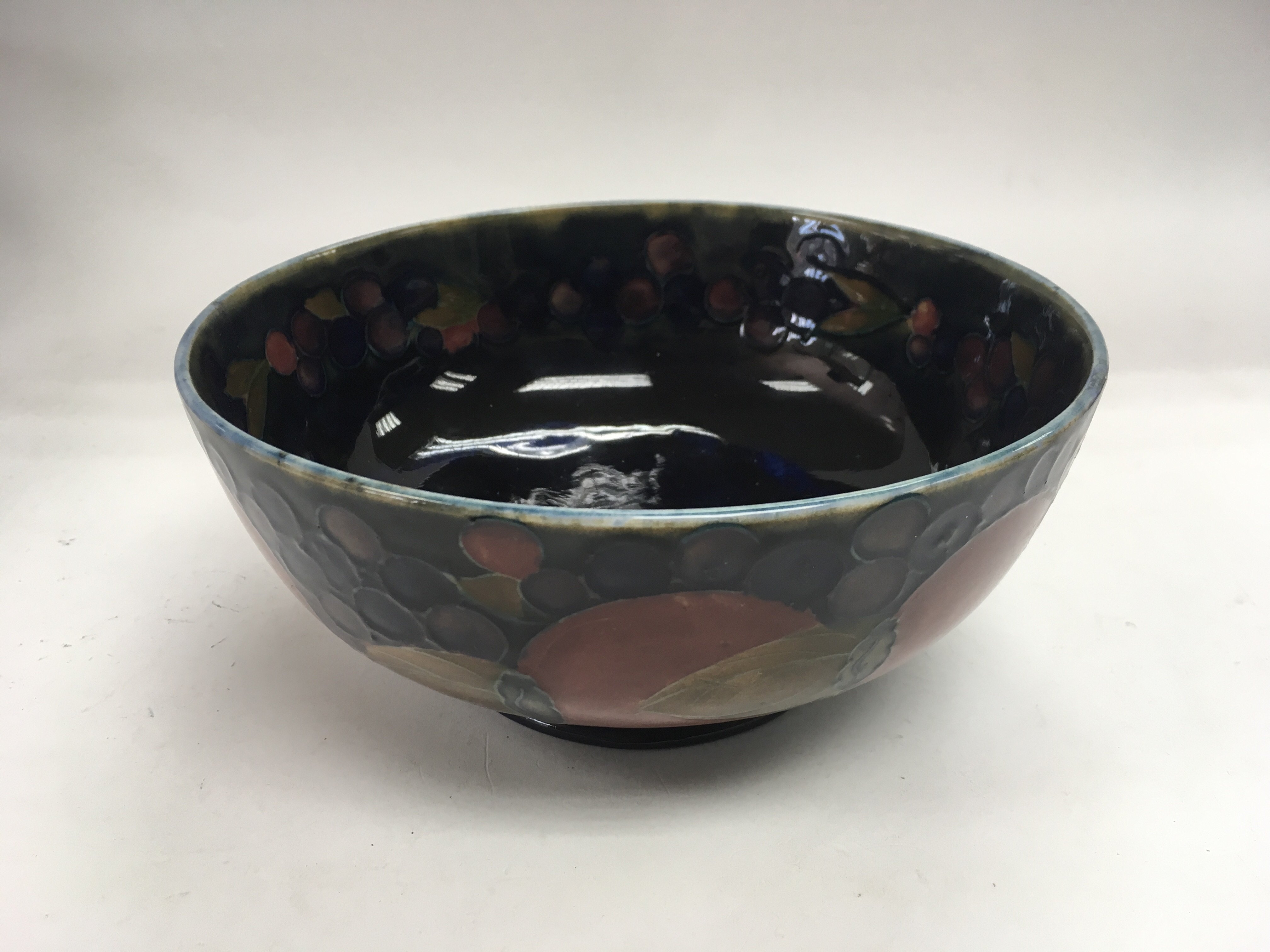 A Moorcroft bowl decorated with fruit on a blue gr