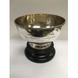 A silver circular bowl raised on a hardwood stand, the bowl bearing inscription for first prize