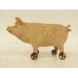 A late 19thC/early 20thC felt covered pig on wheels with squeak, glass eyes and composite snout,