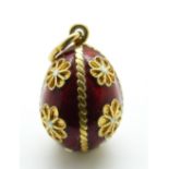 An 18ct gold enamel egg pendant decorated with flowers on a red enamel ground and decorated with