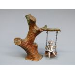 A novelty white metal and cold painted bronze girl on a swing,
