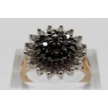 A 9ct gold ring set with black diamonds surrounded by a border of clear diamonds in a large cluster,