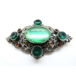 A silver brooch set with a large foiled green cabochon and further green paste and orange paste