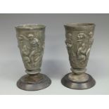 A pair of pewter vases depicting mythical figures, on slate bases,