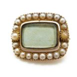 A Victorian mourning brooch set with a border of pearls and a glass compartment to the centre