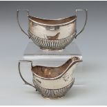 A George V hallmarked silver sugar bowl and milk jug with reeded lower sections,