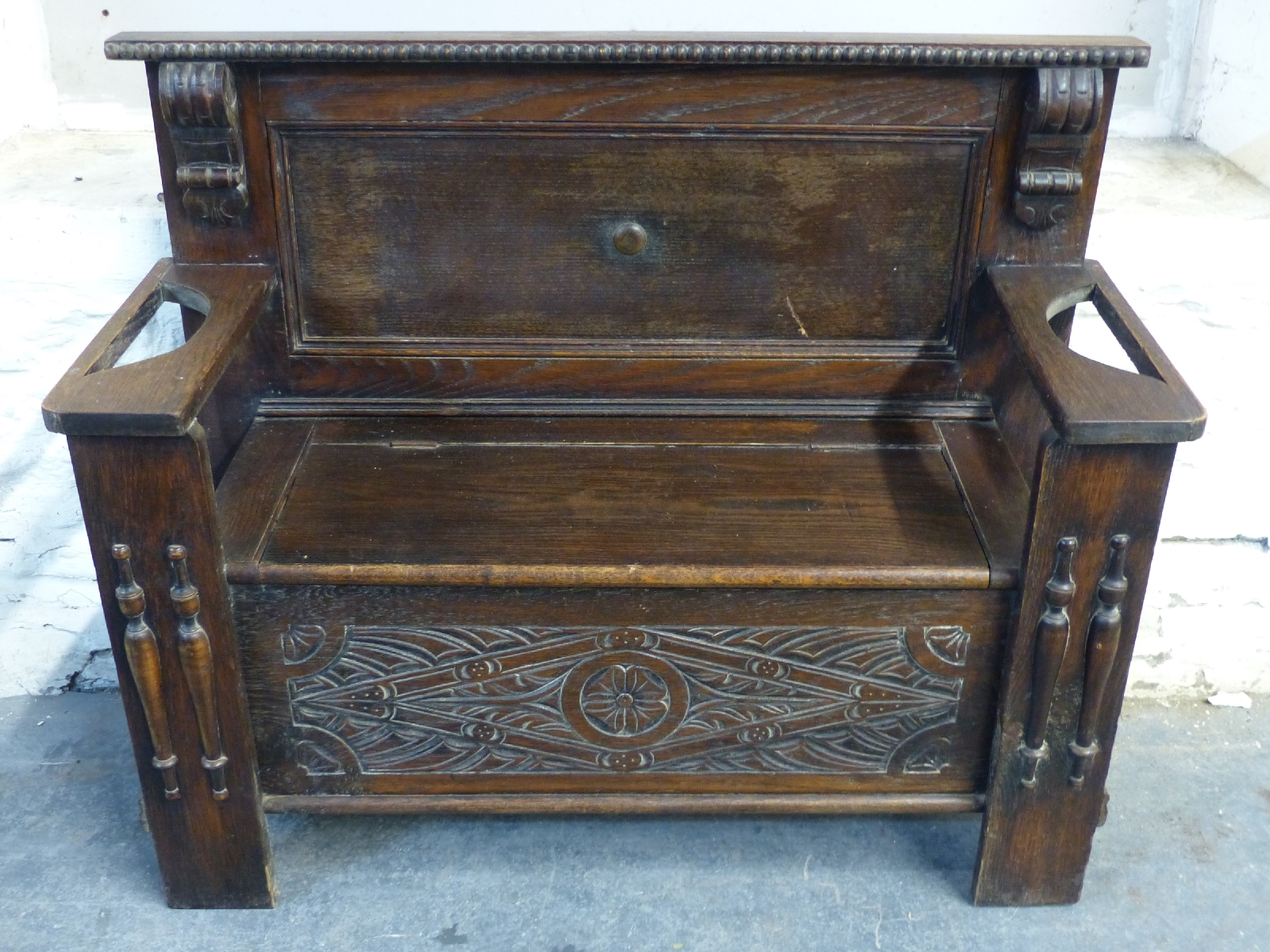 An oak settle with lift up seat and stick stands to arms,