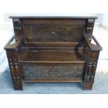 An oak settle with lift up seat and stick stands to arms,