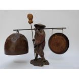 An oriental gong formed as a man holding a cane with bell to one end and gong to other,