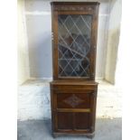 An oak double height corner cupboard with glazed top door,