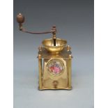 A brass coffee grinder with inset ceramic plaque, embossed decoration and turned wooden handle,