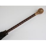 A late 19thC/20thC parasol with spherical yellow metal repoussé decorated handle with cane stick,