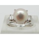 A platinum ring set with a pearl and with an emerald cut diamond to each shoulder, total diamond