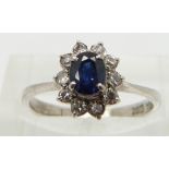 A 14k white gold ring set with an oval sapphire surrounded by diamonds, size L