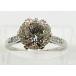 A platinum ring set with a round cut diamond of approximately 2.7ct with diamond encrusted