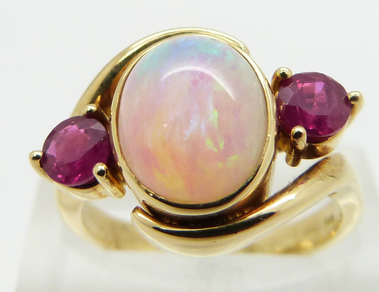 An 18ct gold ring set with an oval opal cabochon and two round cut rubies, size M