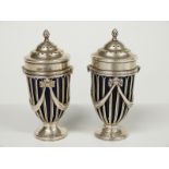 A pair of hallmarked silver pedestal peppers or casters with blue glass liners, swag decoration