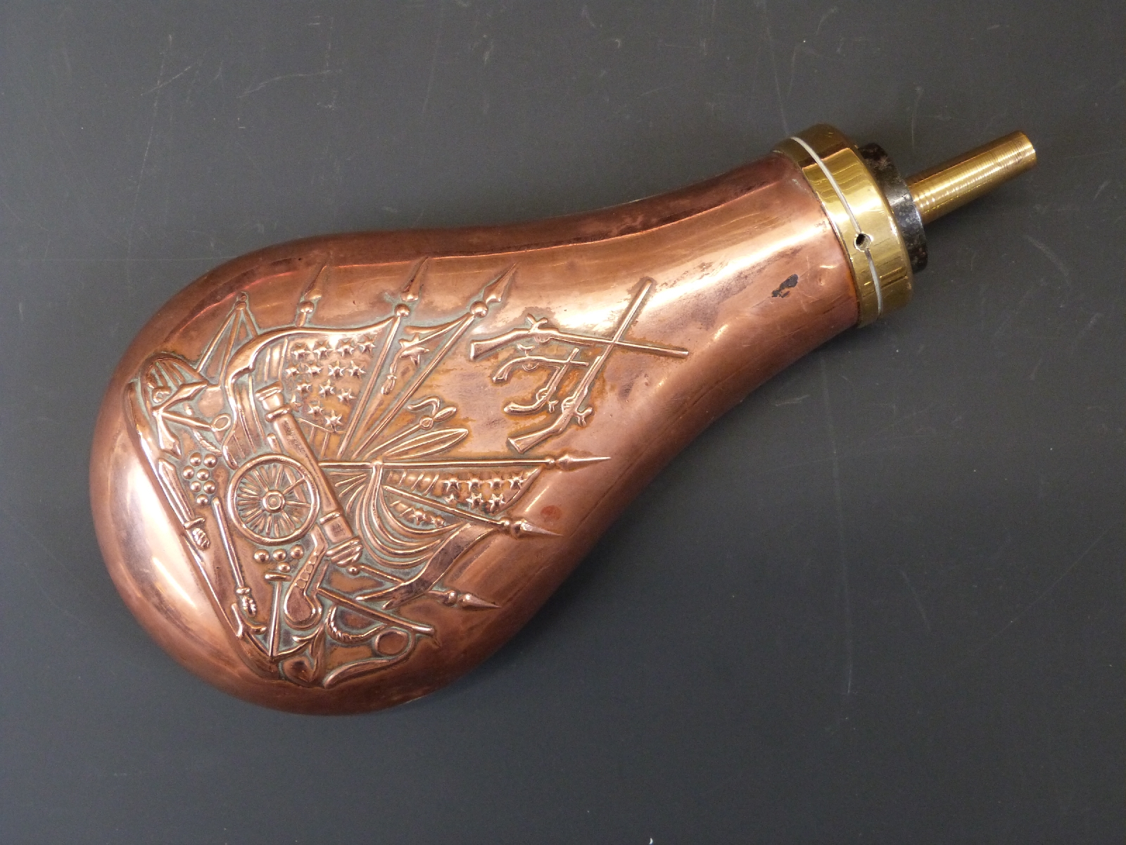 Copper and brass powder flask with embossed decoration of a cannon, guns and flags in the American