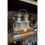 An early 20th century oak and electroplate mounted tantalus, with two glass bottles, one with