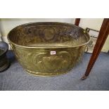 A large Flemish embossed brass oval log bin, with lion mask ring handles, 72cm wide.