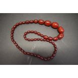 A string of graduated cherry red amber style beads, 74cm, 68g.