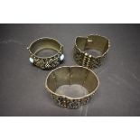 Three large white metal cuff bracelets.