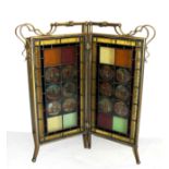 A VICTORIAN BRASS AND STAINED GLASS FIRE SCREEN, the arts and crafts style frame holding magic