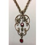 AN EDWARDIAN YELLOW METAL, GARNET AND SEED PENDANT Of scroll design, set with two round cut garnets,